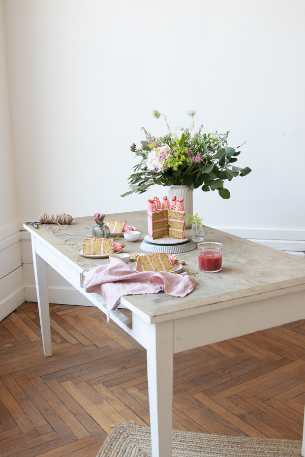 Une scène avec un joli gâteau à étages fraise pistache est composée sur une jolie table en bois